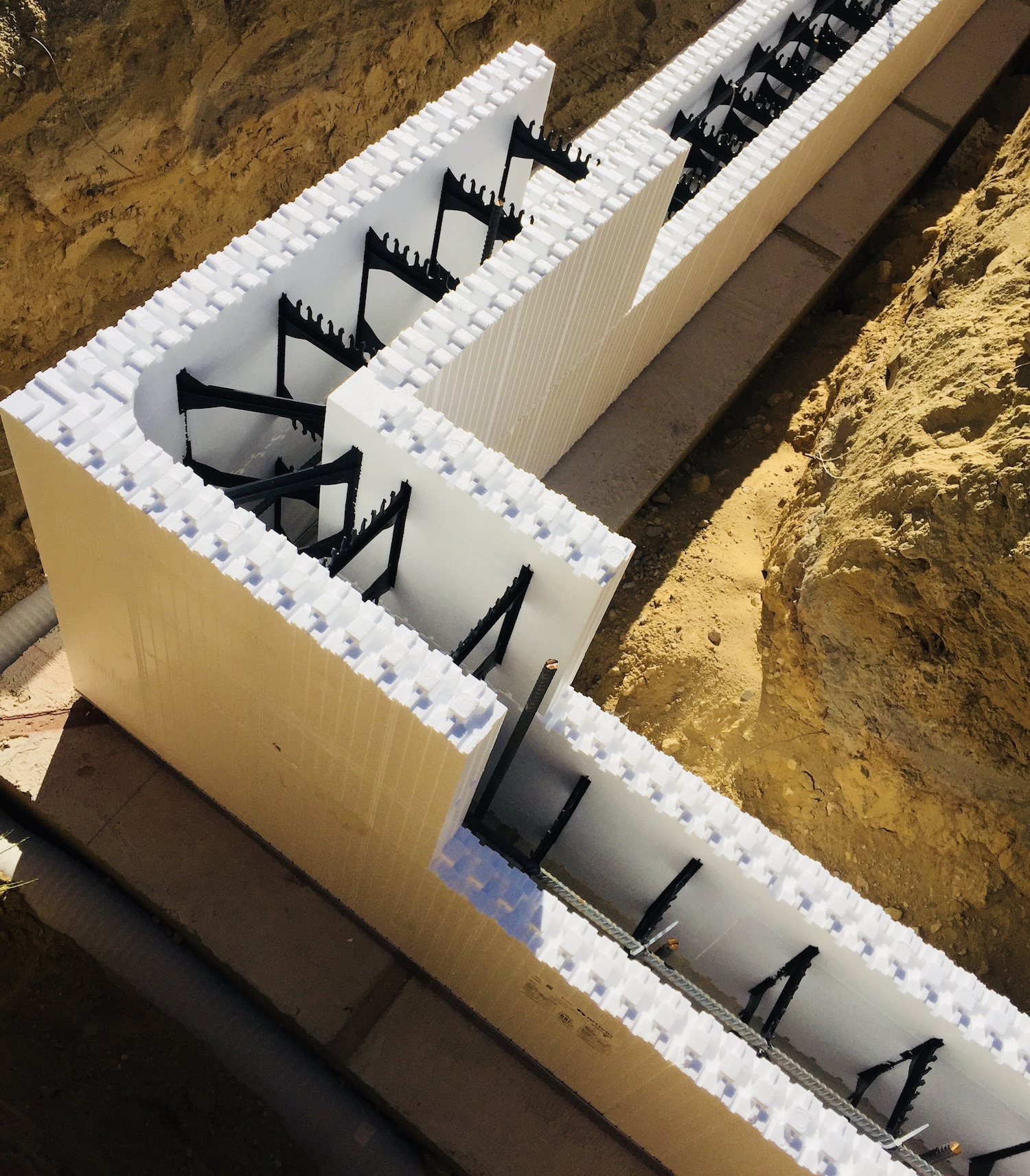 A set of ICF blocks are stacked at the corner of a newly place ICF Foundation. Dirt is seen on both sides of the inner and outer wall