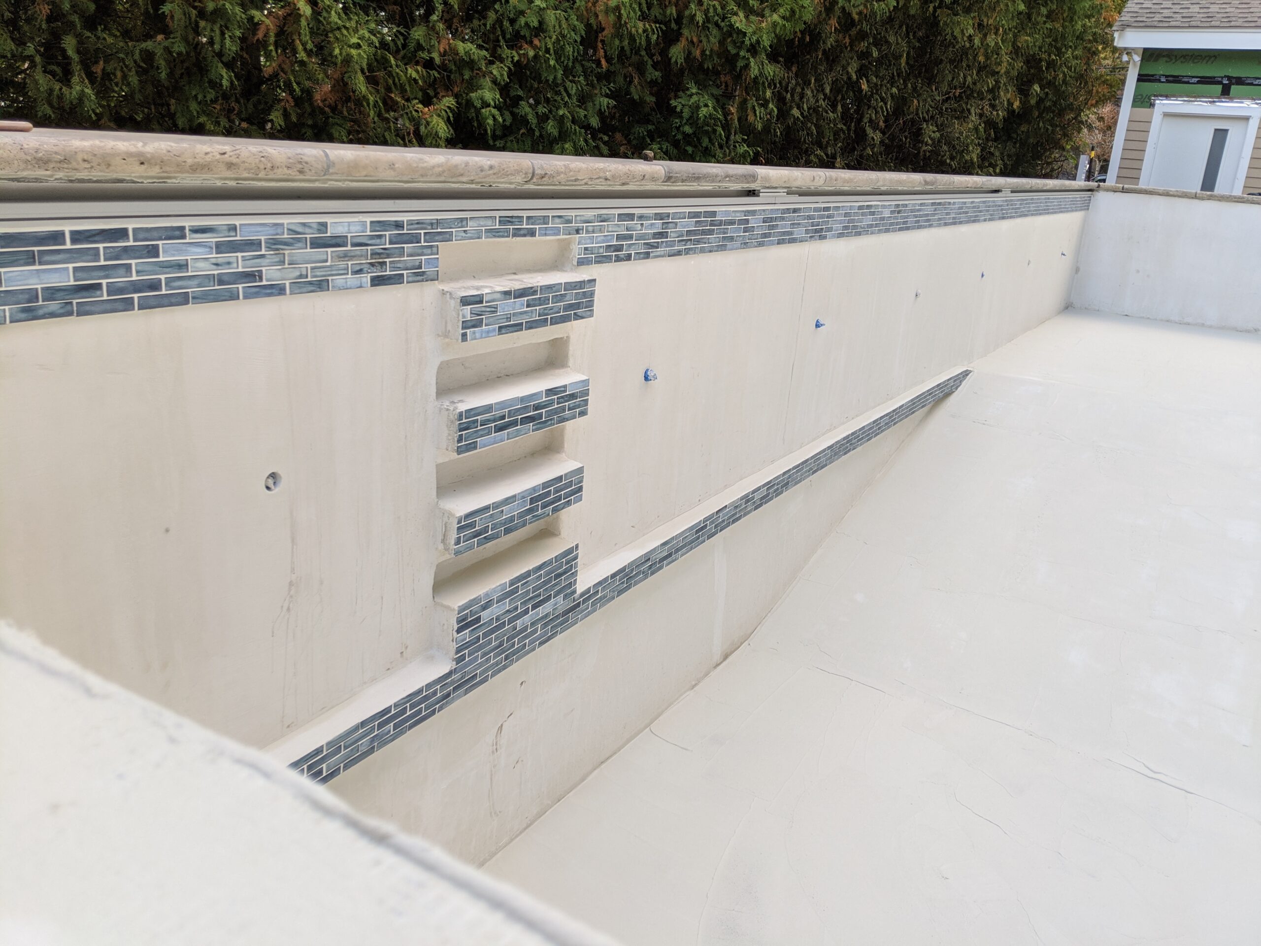 picture of the inside of an ICF pool and a custom built step ladder,built into the wall of the ICF pool with Decorative tiles appearing at the top of the pool and on the fronts of the ladder steps. the rest of the pools is finished with a smooth concrete layer before it will be painted with a waterproofing layer.